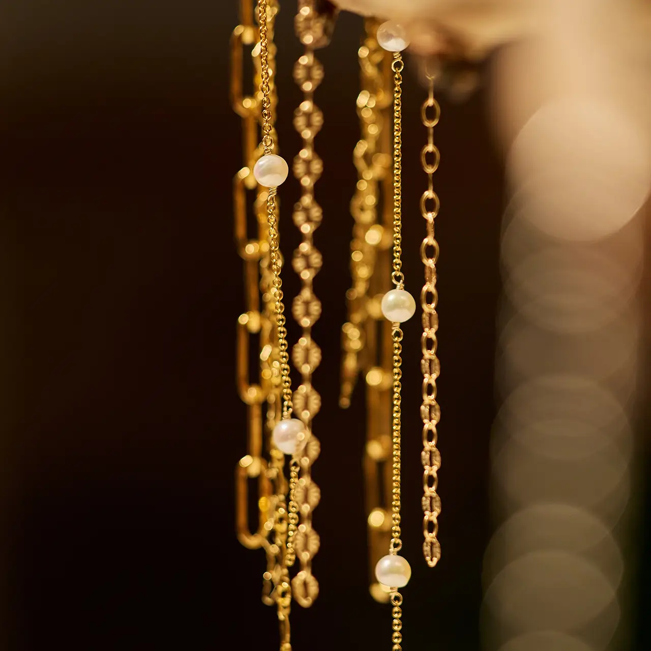 Close-up of elegant gold permanent jewellery chains adorned with delicate pearls, softly illuminated with a warm, golden bokeh background.